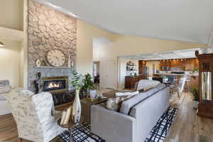 Living area with a stone fireplace, wood finished floors, and high vaulted ceiling
