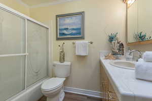 Full bath featuring vanity, enclosed tub / shower combo, crown molding, and dark wood-style floors