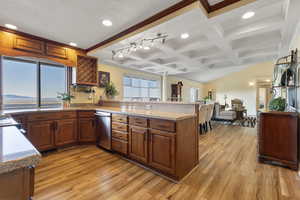 Kitchen with brown cabinetry, a peninsula, coffered ceiling, beam ceiling, and light wood finished floors