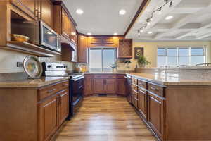 Kitchen with stainless steel appliances, beam ceiling, brown cabinets, coffered ceiling, and a peninsula