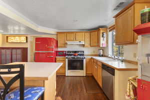 Kitchen featuring light countertops, white range with gas stovetop, dark wood-type flooring, dishwasher, and a textured ceiling