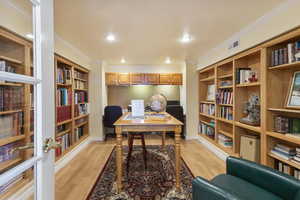 Home office featuring light wood-style floors, ornamental molding, wall of books, a textured ceiling, and built in shelves
