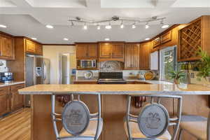 Kitchen featuring brown cabinets, a breakfast bar area, recessed lighting, light stone countertops, and crown molding