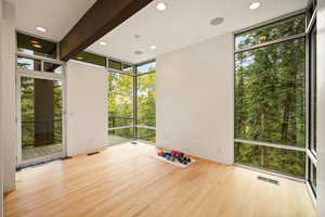 Spare room featuring a wall of windows, light wood-type flooring, recessed lighting, beamed ceiling, and view of wooded area