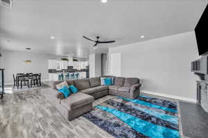 Living area featuring a ceiling fan, recessed lighting, light wood-type flooring, and a fireplace