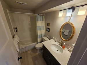 Full bathroom with vanity, dark wood-style flooring, shower / bath combo, and a textured ceiling