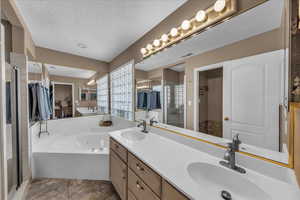 Bathroom featuring double vanity, a stall shower, a garden tub, a spacious closet, and a textured ceiling
