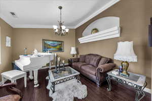 Living area with crown molding, a chandelier, and dark wood finished floors