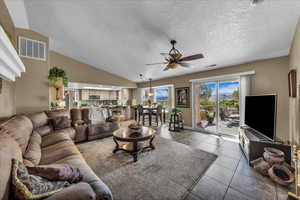 Tiled living area featuring ceiling fan, vaulted ceiling, and a textured ceiling