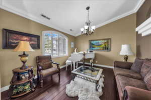 Living area featuring ornamental molding, lofted ceiling, dark wood finished floors, and a chandelier