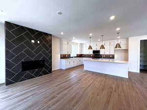 Kitchen featuring a center island with sink, white cabinets, dark wood-type flooring, decorative light fixtures, and open floor plan