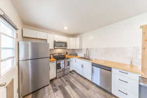 Kitchen with appliances with stainless steel finishes, white cabinets, light wood-style floors, wooden counters, and backsplash