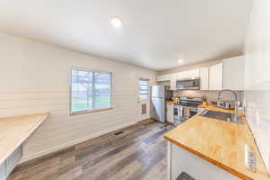 Kitchen featuring butcher block countertops, dark wood-style flooring, white cabinetry, stainless steel appliances, and wood walls