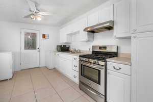 Kitchen featuring stainless steel appliances, white cabinetry, under cabinet range hood, light tile patterned floors, and light countertops