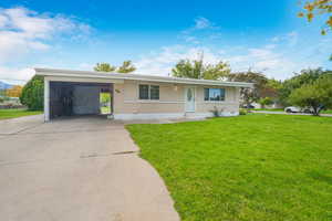 Single story home with a front yard, concrete driveway, an attached carport, and brick siding