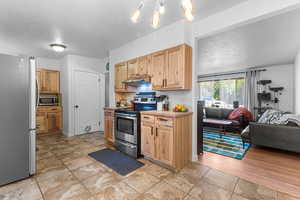Kitchen featuring stainless steel appliances, light countertops, light brown cabinetry, open floor plan, and under cabinet range hood