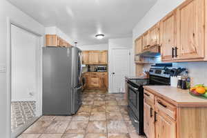 Kitchen with stainless steel appliances, light countertops, under cabinet range hood, decorative backsplash, and light brown cabinetry
