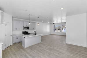 Kitchen with a kitchen island with sink, appliances with stainless steel finishes, pendant lighting, open floor plan, and light wood-style floors