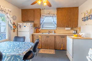 Kitchen featuring light countertops, white appliances, brown cabinetry, and a ceiling fan
