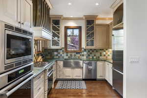 Kitchen featuring appliances with stainless steel finishes, premium range hood, dark stone countertops, decorative backsplash, and recessed lighting