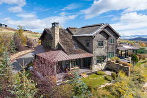 Rear view of property with a standing seam roof, a patio, a metal roof, stone siding, and a chimney