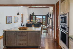 Kitchen with hanging light fixtures, stainless steel appliances, dark wood-style flooring, open floor plan, and a center island