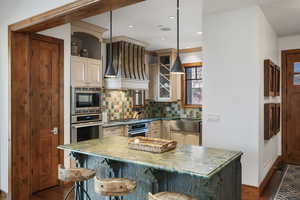 Kitchen with glass insert cabinets, backsplash, a center island, custom range hood, and stainless steel appliances