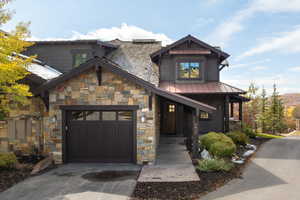 Craftsman-style house with a metal roof, driveway, stone siding, a standing seam roof, and an attached garage
