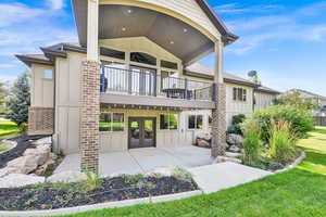 Rear view of house featuring board and batten siding, french doors, a balcony, a patio area, and a lawn