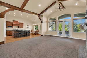 Living area featuring french doors, high vaulted ceiling, beam ceiling, light colored carpet, and a chandelier