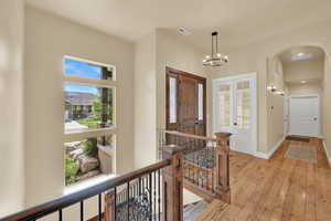 Entrance foyer with french doors, light wood-style floors, arched walkways, and a chandelier