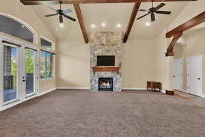 Unfurnished living room with a ceiling fan, high vaulted ceiling, a stone fireplace, carpet floors, and beamed ceiling