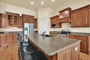 Kitchen with light wood-style flooring, stainless steel appliances, dark stone counters, glass insert cabinets, and premium range hood