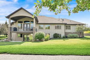 Rear view of house featuring board and batten siding, a lawn, a balcony, and a shingled roof