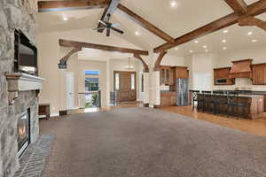 Living room with arched walkways, beamed ceiling, a stone fireplace, high vaulted ceiling, and light colored carpet