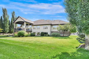 Back of house featuring a yard, a shingled roof, a balcony, brick siding, and board and batten siding