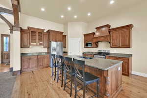Kitchen with brown cabinetry, dark stone counters, a kitchen breakfast bar, stainless steel appliances, and light wood-style floors
