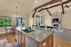 Kitchen featuring brown cabinetry, light stone counters, beam ceiling, stainless steel dishwasher, and a fireplace