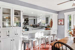 Kitchen featuring white cabinetry, a breakfast bar area, open shelves, glass insert cabinets, and stainless steel range with electric cooktop