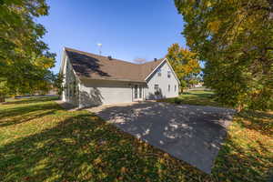 View of side of property featuring a lawn, a patio, roof with shingles, and driveway