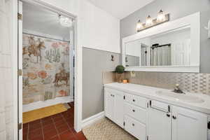 Bathroom featuring vanity, dark tile patterned flooring, a shower with shower curtain, and tasteful backsplash