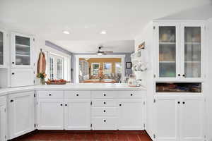 Kitchen with glass insert cabinets, white cabinetry, light countertops, recessed lighting, and ceiling fan