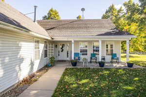 View of exterior entry featuring a fronot porch, lawn and roof with shingles