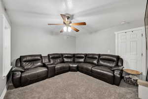 Living room/family room with a textured ceiling, carpet flooring, and ceiling fan