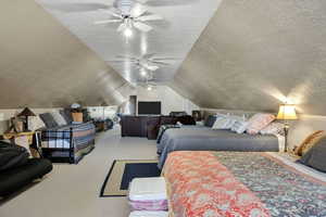 Carpeted living room/loft area featuring a textured ceiling, vaulted ceiling, and a ceiling fan