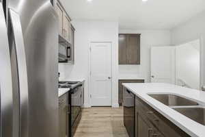 Kitchen featuring black appliances, light wood-style floors, recessed lighting, dark brown cabinets, and light stone counters