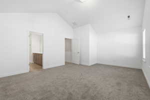 Unfurnished bedroom featuring high vaulted ceiling, light colored carpet, and ensuite bath