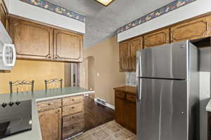 Kitchen featuring freestanding refrigerator, black electric cooktop, a textured ceiling, arched walkways, and brown cabinets