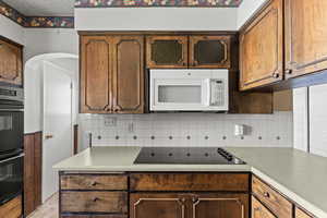 Kitchen featuring decorative backsplash, black appliances, and light countertops