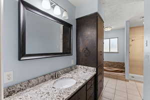 Bathroom with vanity, light tile patterned floors, a textured ceiling, and a stall shower